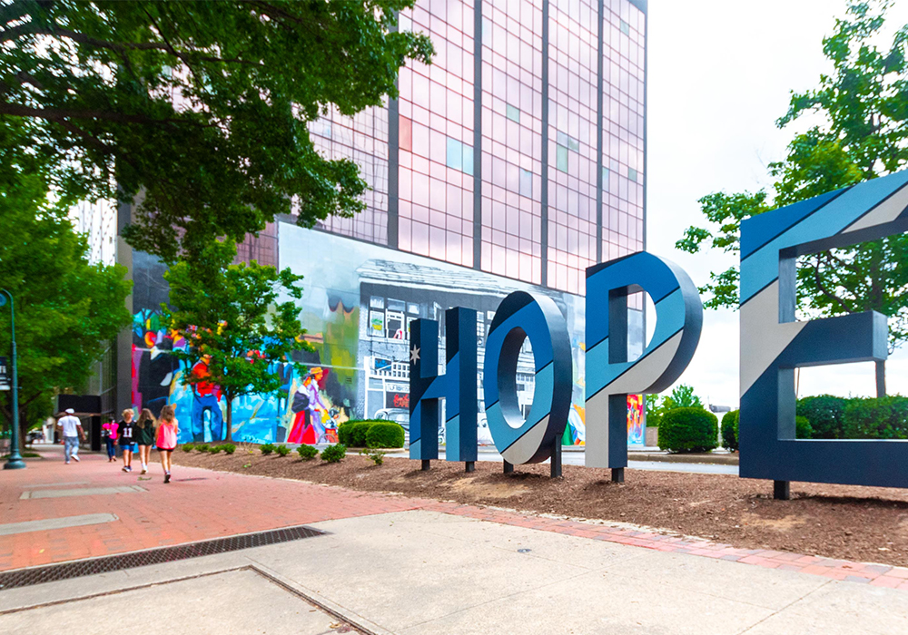 A sidewalk in Columbia with large letters spelling out Hope and people walking in front of a mural.